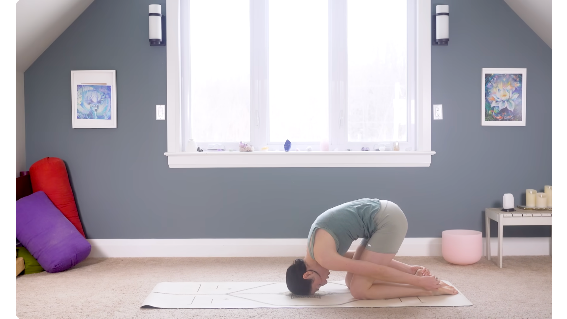 Woman kneeling on a mat and rounding her body forward in Rabbit Pose